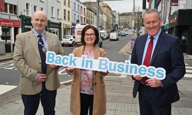 finance minister conor murphy stands with two members of omagh chamber holding a sign saying back in business